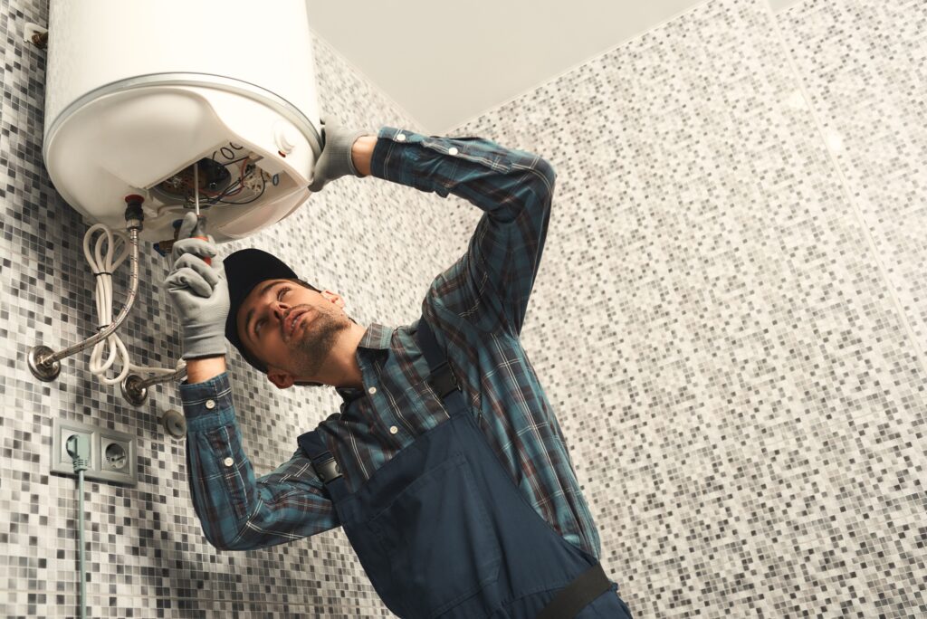 Plumber installing electric heating boiler. Young handyman in uniform setting up electric heating
