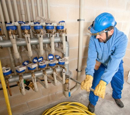 A technician works on plumbing valves in a utility room during the day