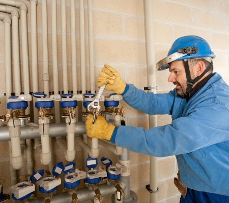 A technician works on plumbing valves in a utility room during the day