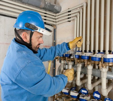 A technician works on plumbing valves in a utility room during the day
