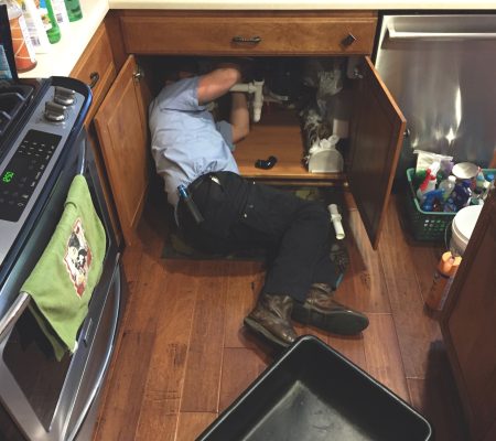 Man working under the kitchen sink fixing the plumbing.