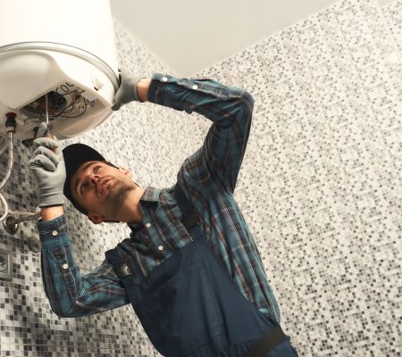 Plumber installing electric heating boiler. Young handyman in uniform setting up electric heating